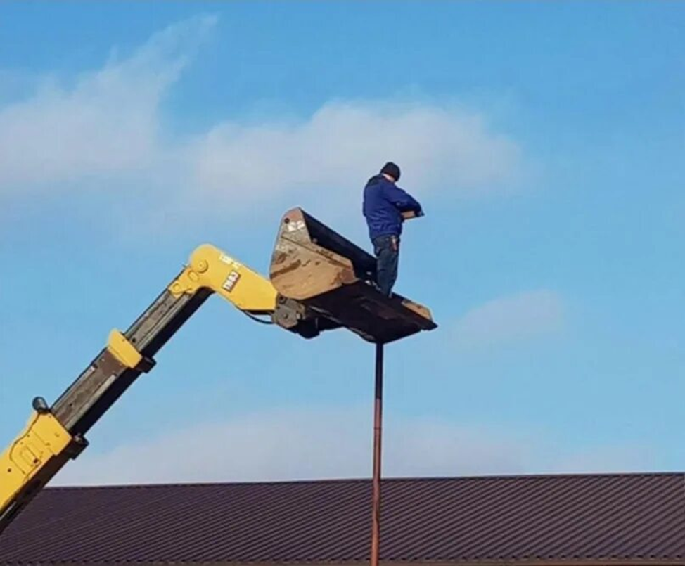 Работник стоит в ковше погрузчика на высоте